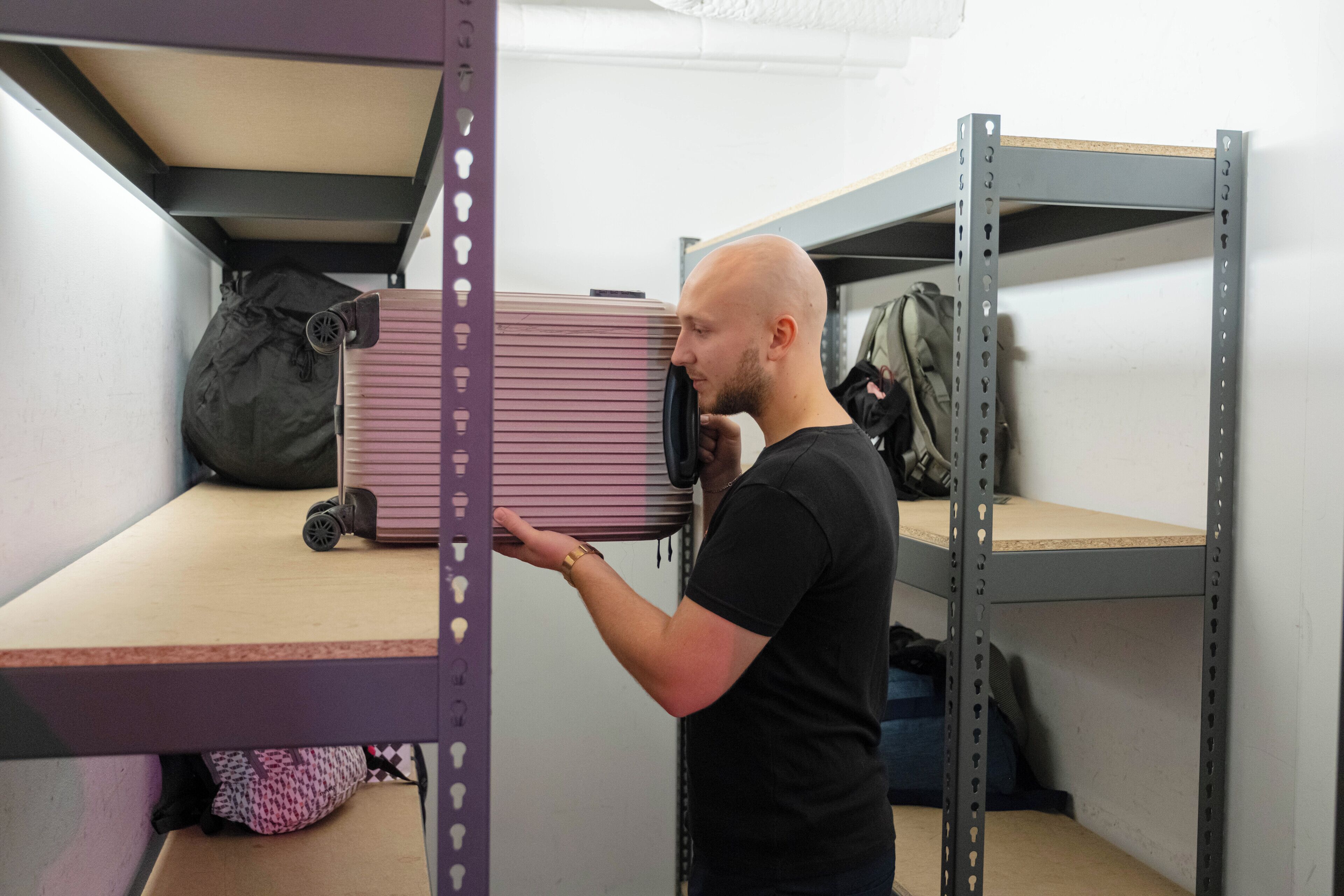 A person standing in a storage area with metal shelving units, a suitcase, and a backpack.