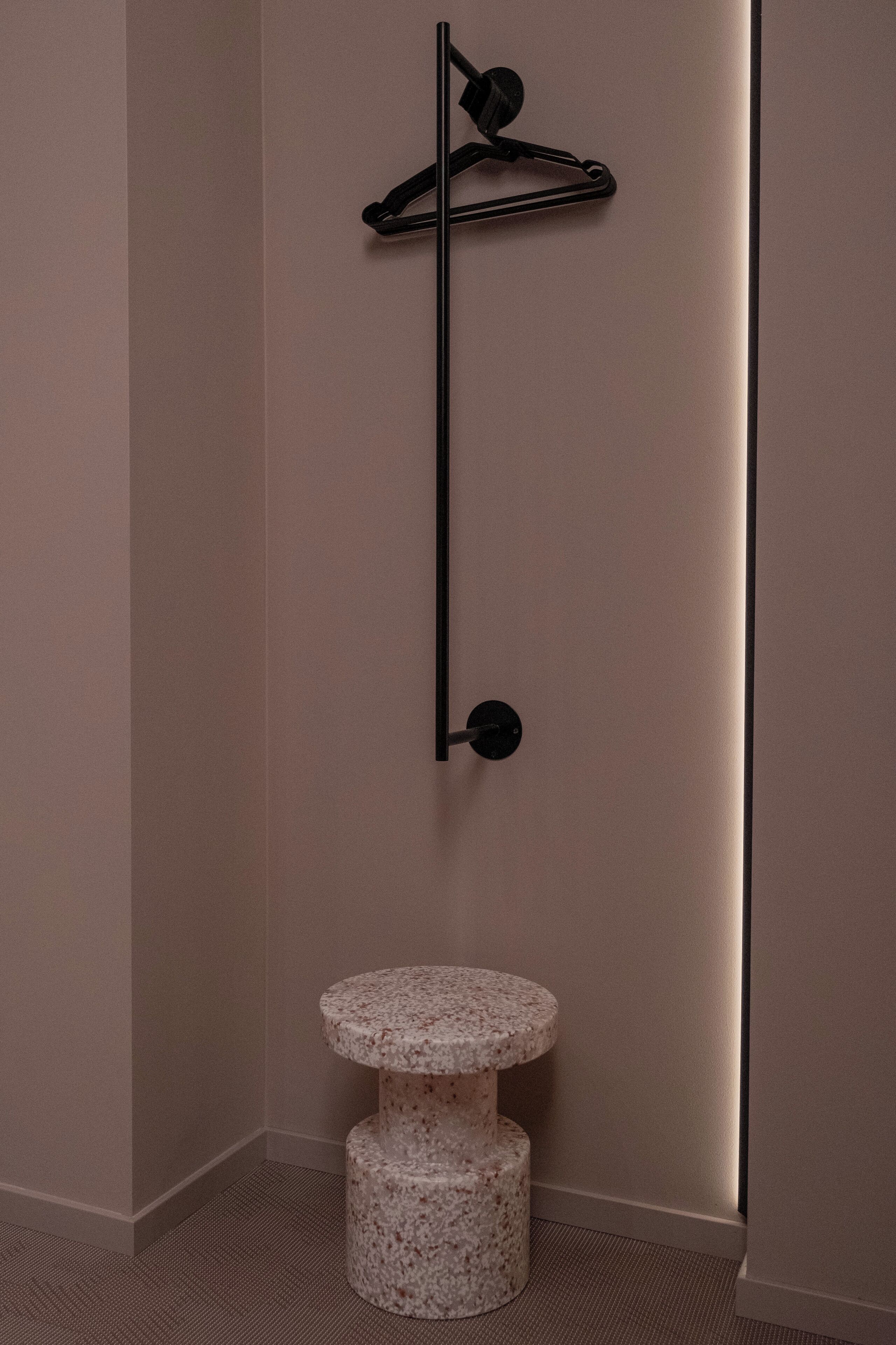 A corner of a room with a wall-mounted black shelf and a two-tiered marble pedestal table.
