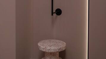 A corner of a room with a wall-mounted black shelf and a two-tiered marble pedestal table.