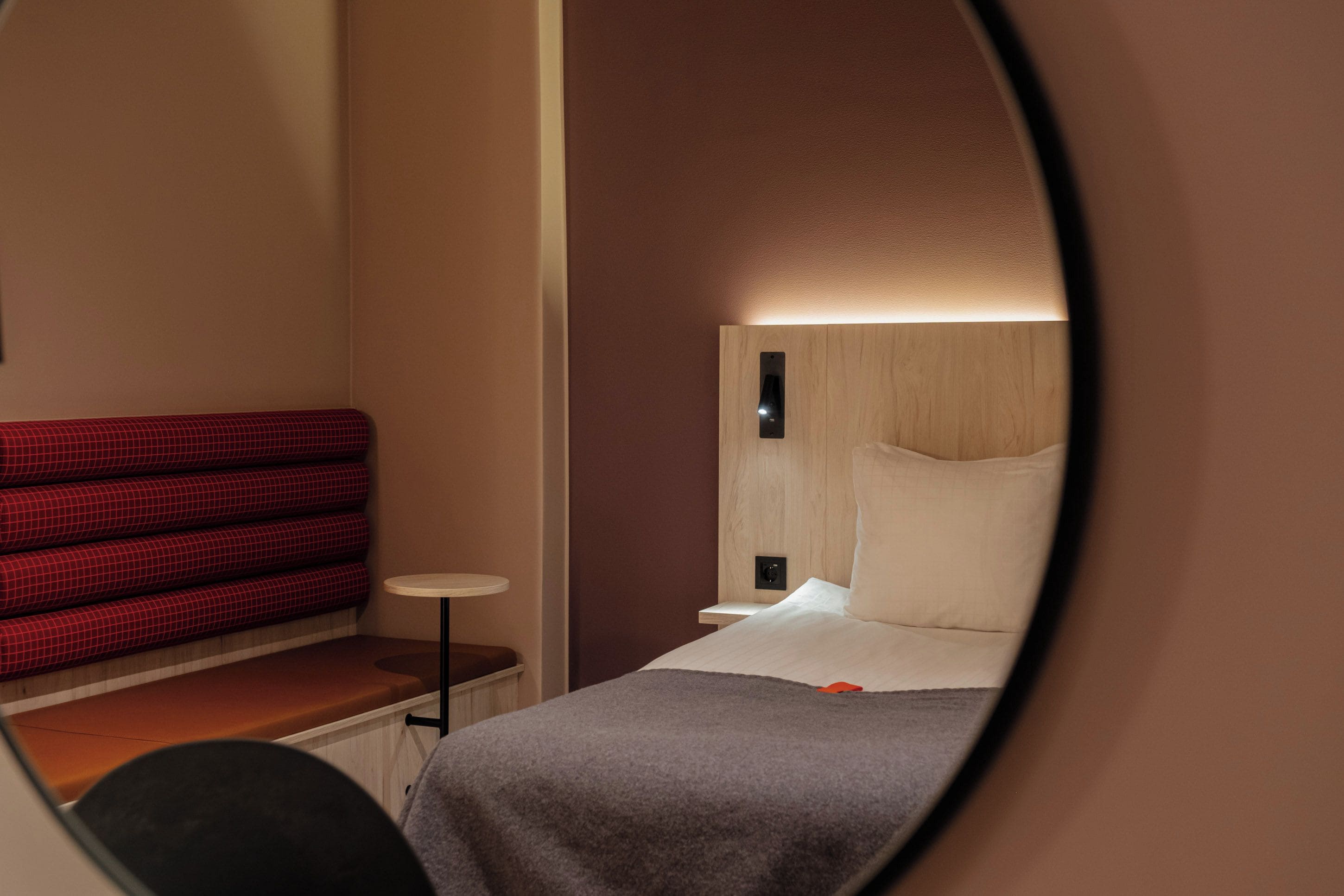Una habitación de hotel con una cama, un sofá rojo a cuadros, una mesita redonda y una mesita de noche.