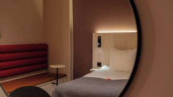 Una habitación de hotel con una cama, un sofá rojo a cuadros, una mesita redonda y una mesita de noche.