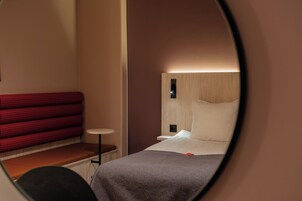 Una habitación de hotel con una cama, un sofá rojo a cuadros, una mesita redonda y una mesita de noche.