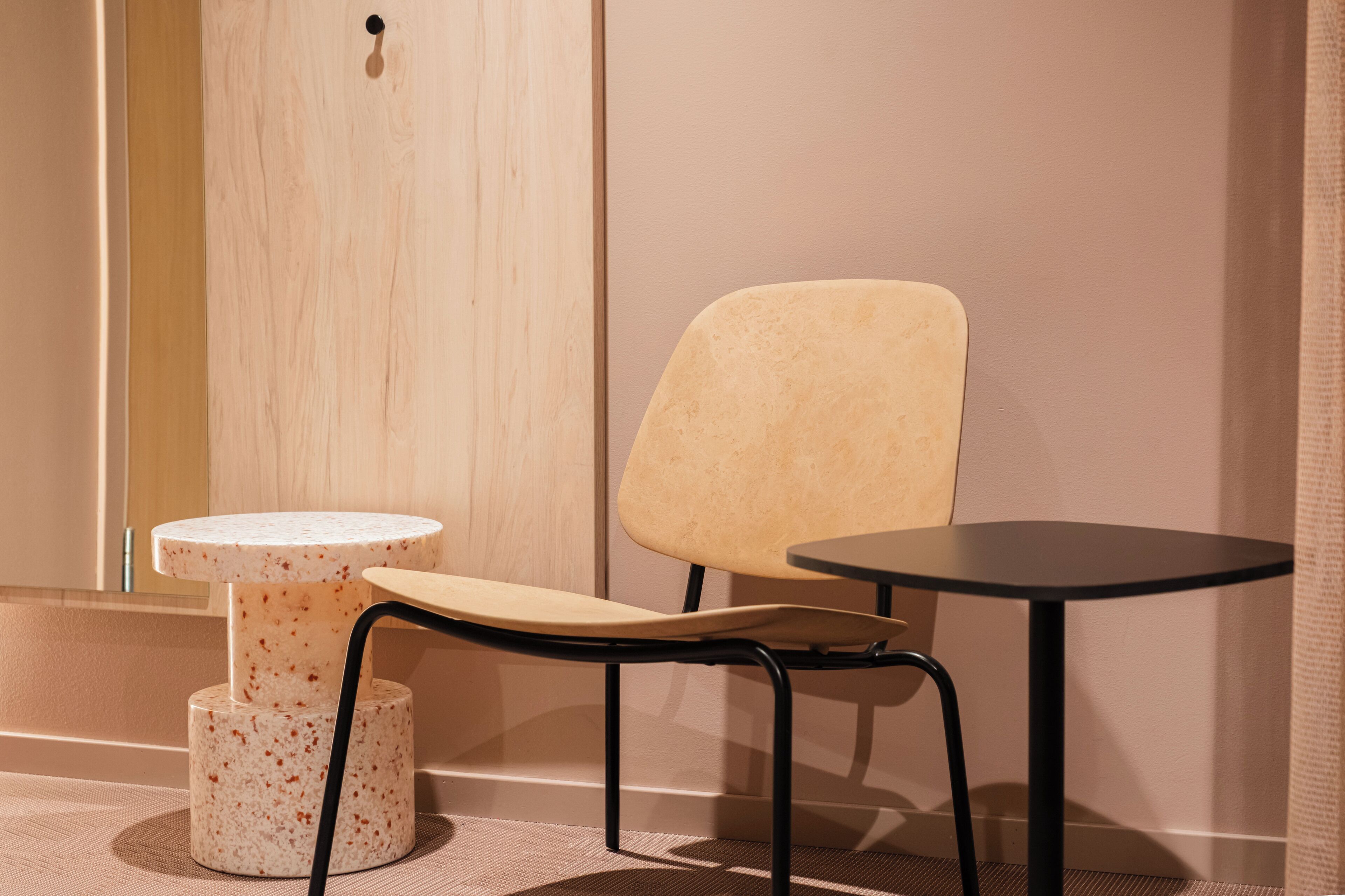 Een kamer met een houten deur, een beige stoel, een klein rond tafeltje en een groter rond tafeltje.