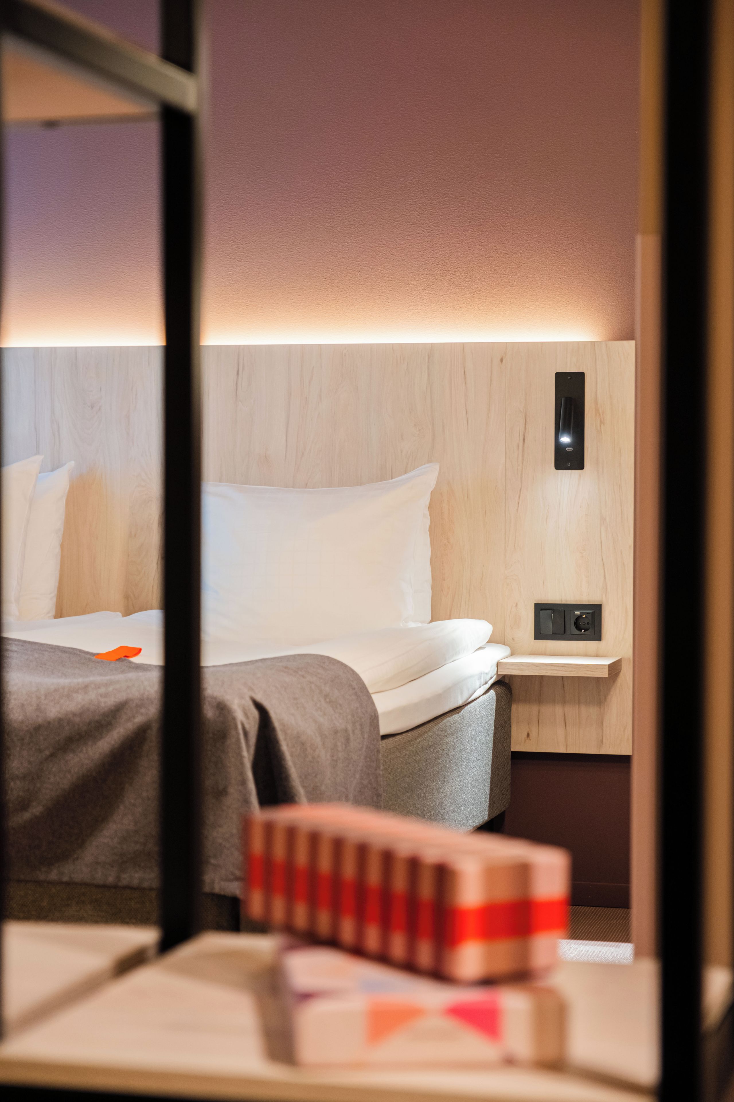 A hotel room with a bed, a bedside table with a lamp, and a wall-mounted power outlet.