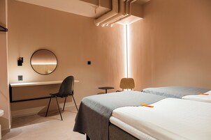 Habitación de hotel con escritorio, dos camas, una silla y un espejo redondo.