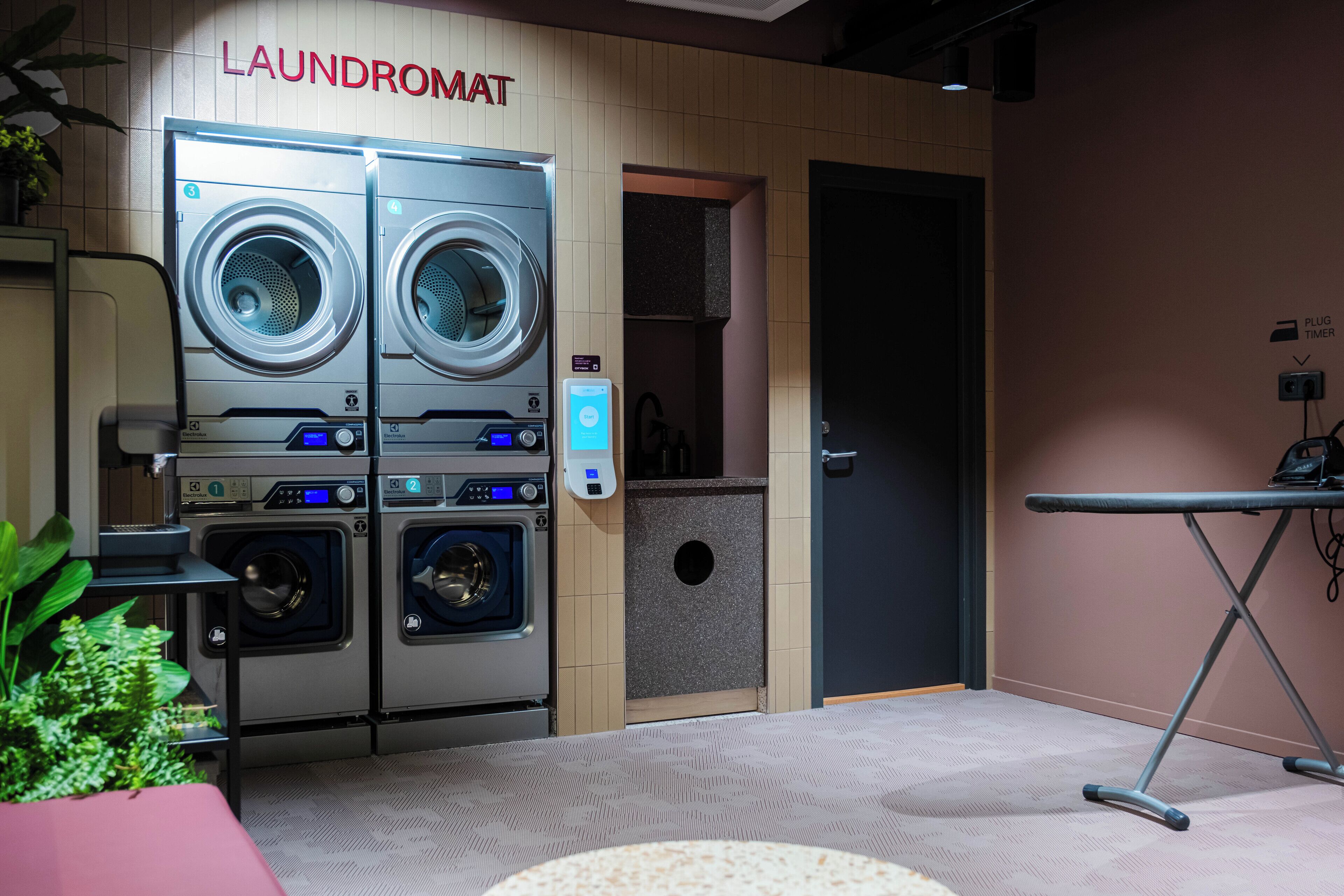 A laundromat with two stacked washing machines and dryers, a control panel, and a sign indicating a plug timer.