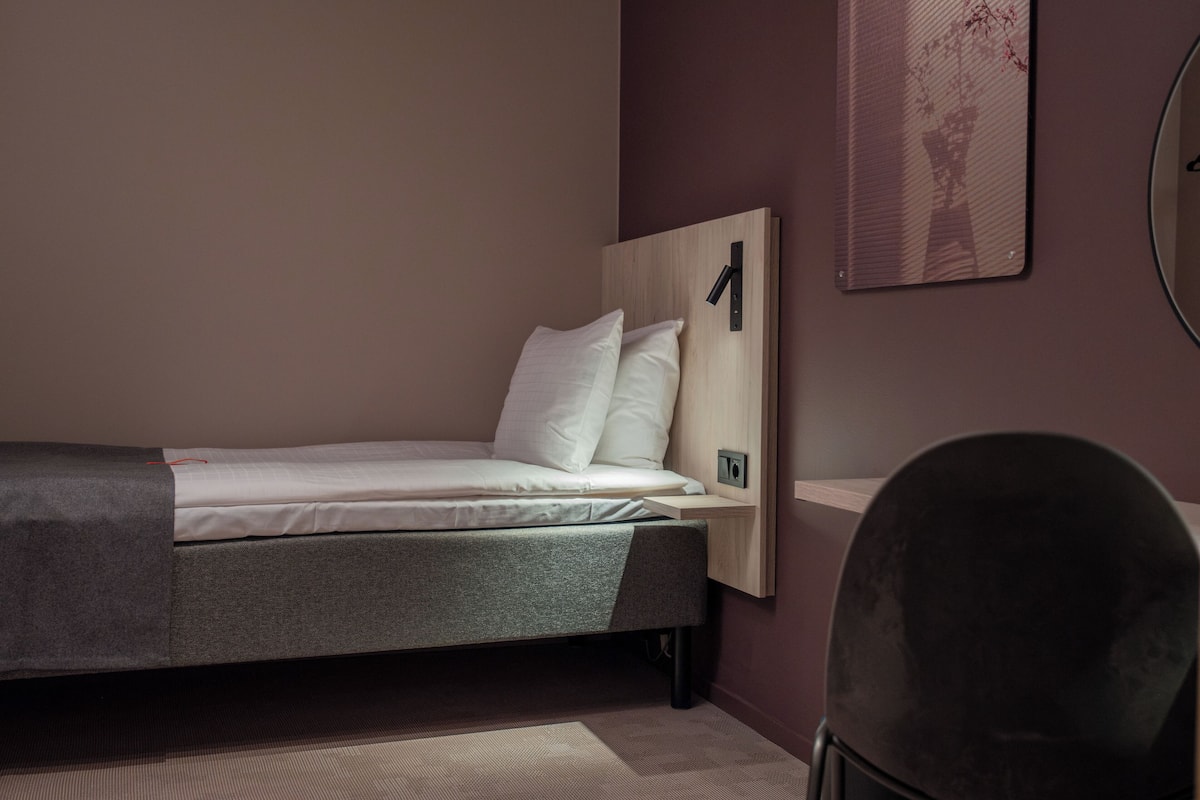 A single bed with a wooden headboard, a bedside table, and a wall-mounted clock.