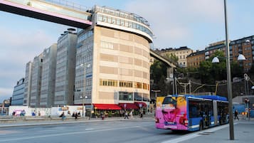 A bus with a large advertisement on its back, a pedestrian overpass, and a building with multiple floors and large windows.