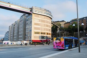 Ein Bus mit einer großen Werbung auf der Rückseite, einer Fußgängerbrücke und einem mehrstöckigen Gebäude mit großen Fenstern.