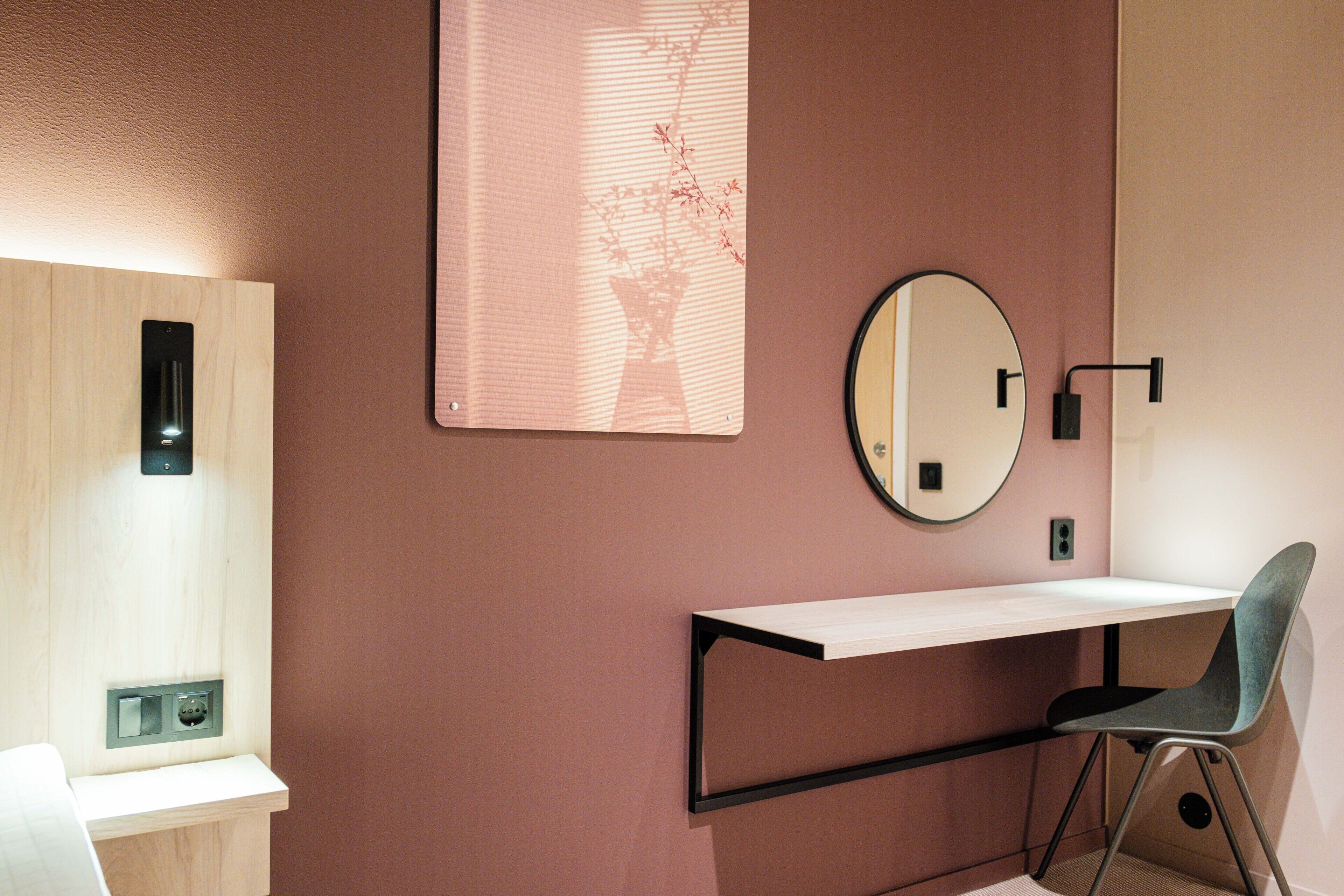 Una habitación moderna con un escritorio de madera, un espejo redondo y una lámpara de pared.