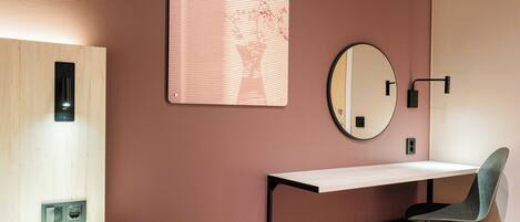 Una habitación moderna con un escritorio de madera, un espejo redondo y una lámpara de pared.