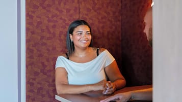 Una persona sentada a una mesa con un fondo de papel tapiz estampado.