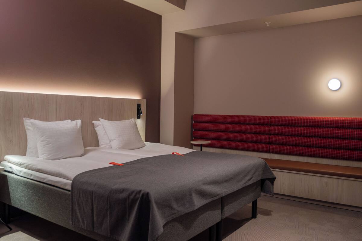 A modern hotel room with a bed, a bench, and a red checkered headboard.