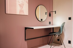 Una habitación con un escritorio, una silla, un espejo redondo y una lámpara fijada a la pared.