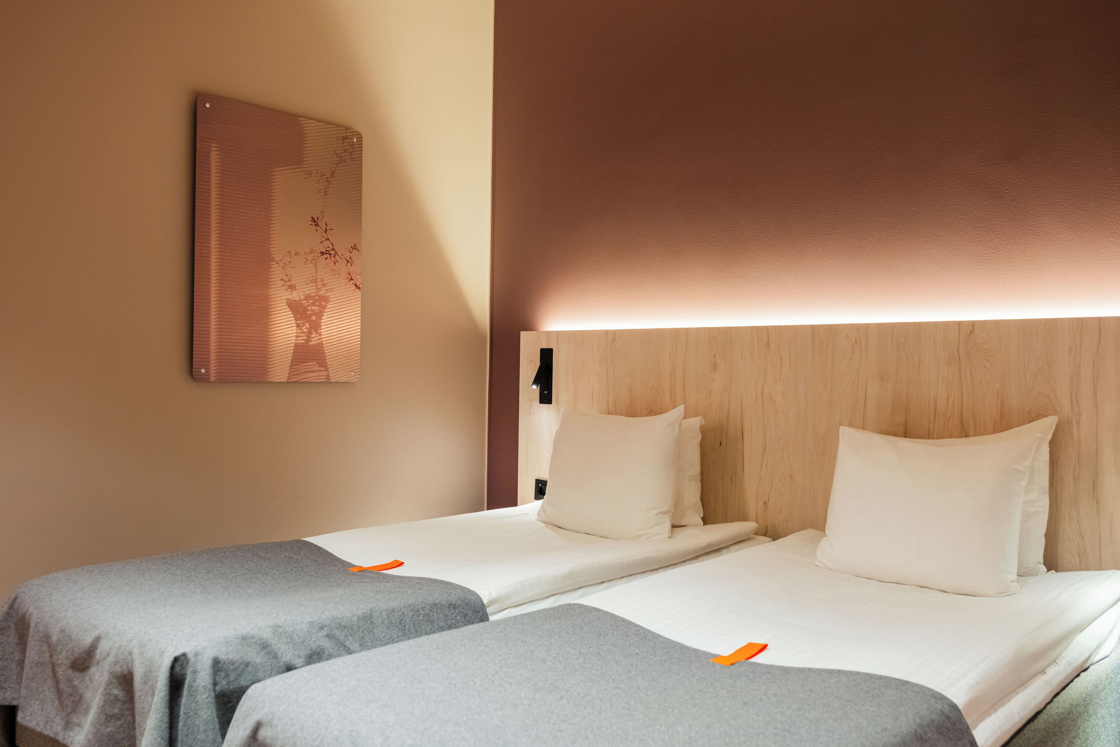 A hotel room with two single beds, a wooden headboard, a wall-mounted artwork, and a bedside table.
