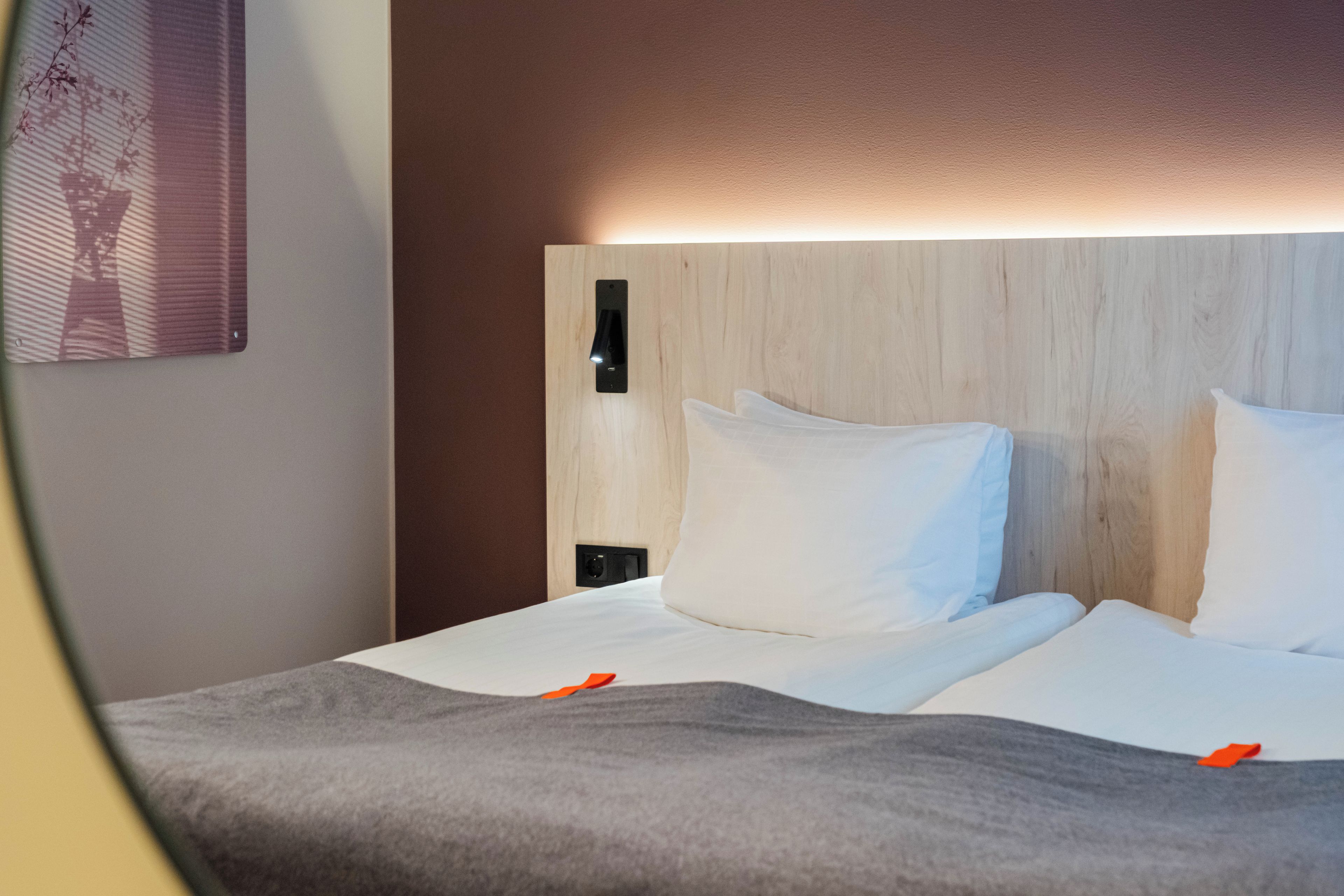 Habitación de hotel con cama, mesita de noche y lámpara de pared.