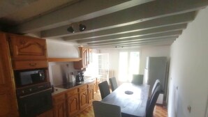 Een keuken met houten kastjes, een magnetron en een koffiezetapparaat. Er is een eettafel met stoelen.