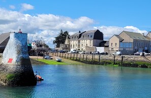 A waterfront area with a stone tower, a row of parked cars, and buildings with varying architectural styles.