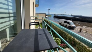 A balcony with a table and chairs, overlooking a waterfront with a van parked nearby. - 2-room garage facing with panoramic view of the sea and TATIHOU island (UNESCO) (Saint-Vaast-la-Hougue)
