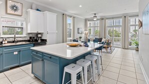 A modern kitchen with a central island, bar stools, and a dining area with a view of the city. - Tidal Charm by AvantStay | Walk to Beach, Community Pool, Balcony, Ocean Views (Panama City Beach)