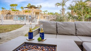 A patio area with a white table, two bottles of wine, and a glass of water on a coaster. - Sleeps 18 | Luxe 30A Beach Home w/ Resort Pool + Outdoor Fireplace (Santa Rosa Beach)