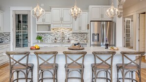 A kitchen with white cabinets, a large island with bar stools, stainless steel appliances, and a decorative backsplash. - Sleeps 18 | Luxe 30A Beach Home w/ Resort Pool + Outdoor Fireplace (Santa Rosa Beach)