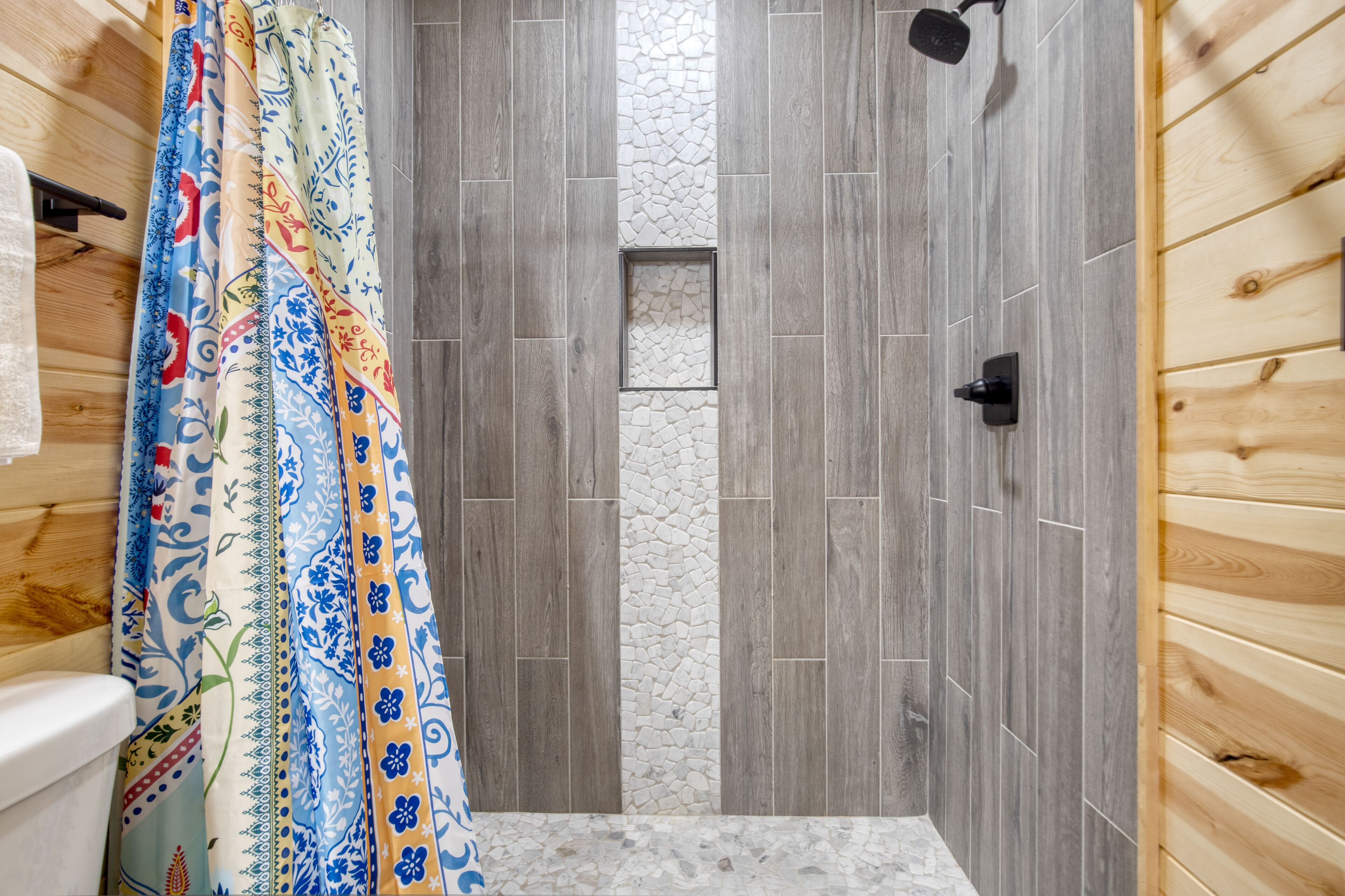 Un espace douche agrémenté d’un rideau de douche à motifs, de murs en bois et d’un mur d’accent en pierre.