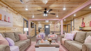 A cozy room with wooden walls and ceiling, two sofas with pink cushions, a coffee table with decorative items, and a ceiling fan. - Designer Retreat • Pool + Theater + Hot Tub • Near Pigeon Forge | Pink Pines (Sevierville)