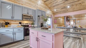 A modern kitchen with grey and pink cabinets, stainless steel appliances, and a central island. - Designer Retreat • Pool + Theater + Hot Tub • Near Pigeon Forge | Pink Pines (Sevierville)