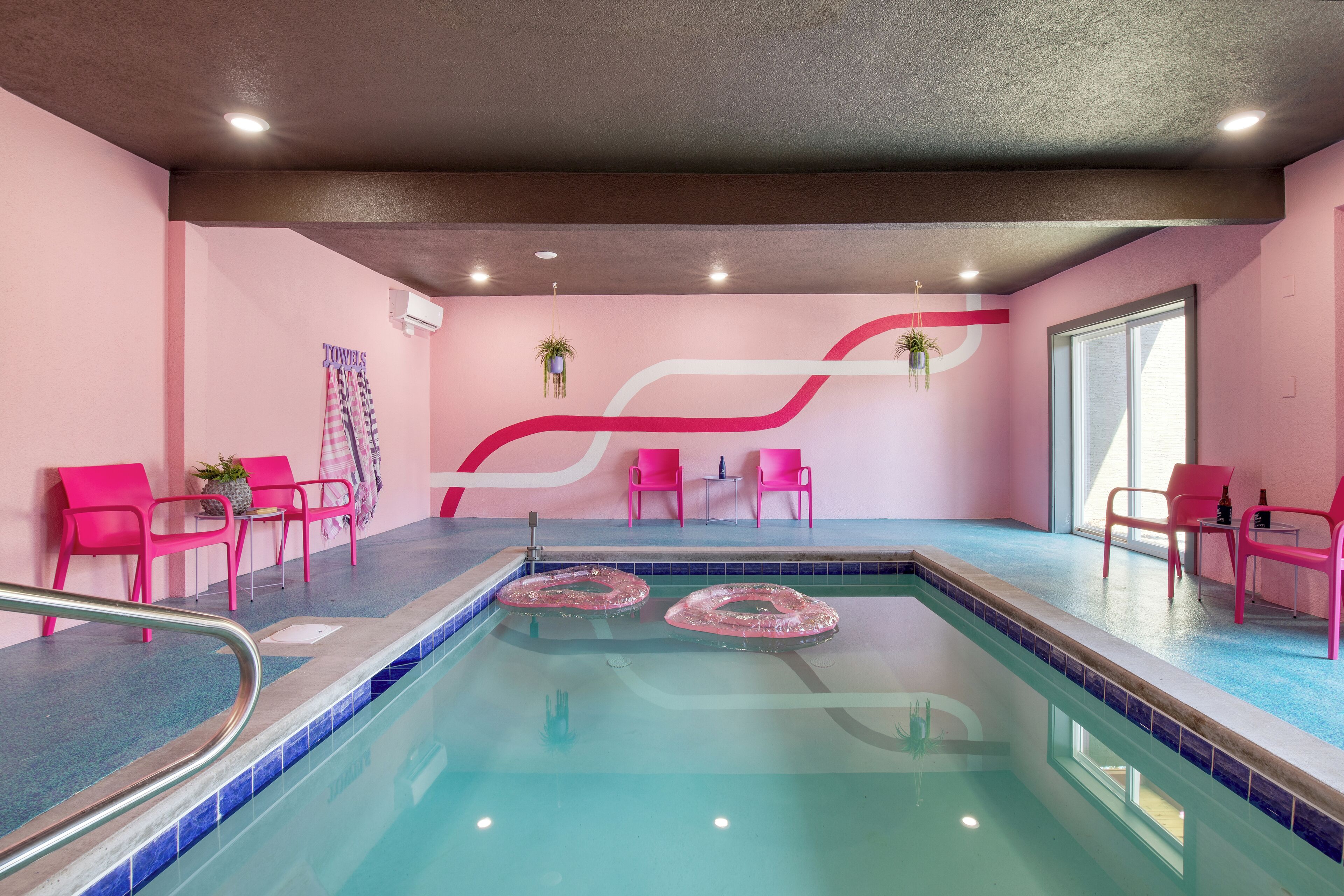 A swimming pool area with pink chairs and a red and white wall design.