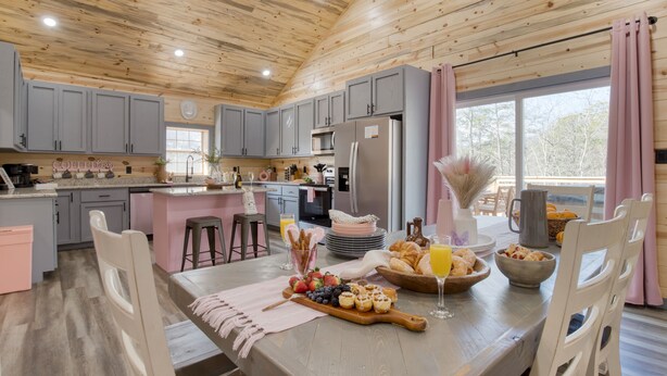 A modern kitchen with grey cabinets, a wooden ceiling, and a breakfast setup on the island. - Designer Retreat • Pool + Theater + Hot Tub • Near Pigeon Forge | Pink Pines (Sevierville)