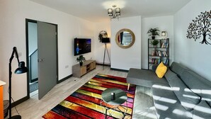 A modern living room with a sofa, a colorful striped rug, a television, a bookshelf, and a decorative tree wall art. - Sandringham House Contractors, Families, Holidays (Cleethorpes)