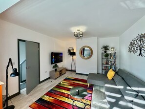 A modern living room with a sofa, a colorful striped rug, a television, a bookshelf, and a decorative tree wall art. - Sandringham House Contractors, Families, Holidays (Cleethorpes)
