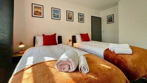 A hotel room with two beds, a nightstand with a lamp, and wall art depicting Egypt, India, and a beach. - Sandringham House Contractors, Families, Holidays (Cleethorpes)