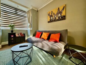 A living room with a sofa, a coffee table, a side table, a bookshelf, and a painting on the wall.