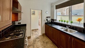 A kitchen with wooden cabinets, a black countertop, a stove, a sink, a window with plants, and a pendant light.