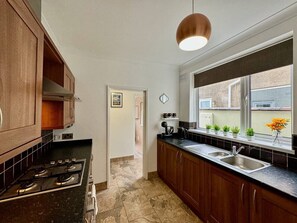 A kitchen with wooden cabinets, a black countertop, a stove, a sink, a window with plants, and a pendant light.