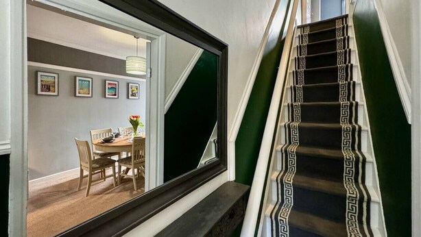 A staircase with a black and white patterned carpet, a dining area with a table and chairs, and a mirror reflecting the room.