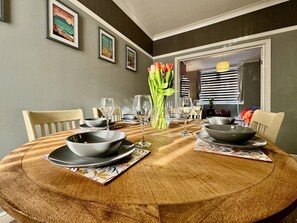 A round dining table with plates, bowls, and glasses, set in a room with framed pictures on the wall and a door leading to another area.