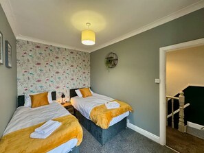 A room with two beds, a small table, a wall clock, and a door leading to another room.