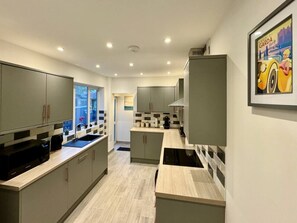 A modern kitchen with grey cabinets, a black microwave, and a tiled backsplash.