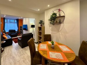 A modern living room with a sofa, a dining table with chairs, a TV, and a bookshelf.