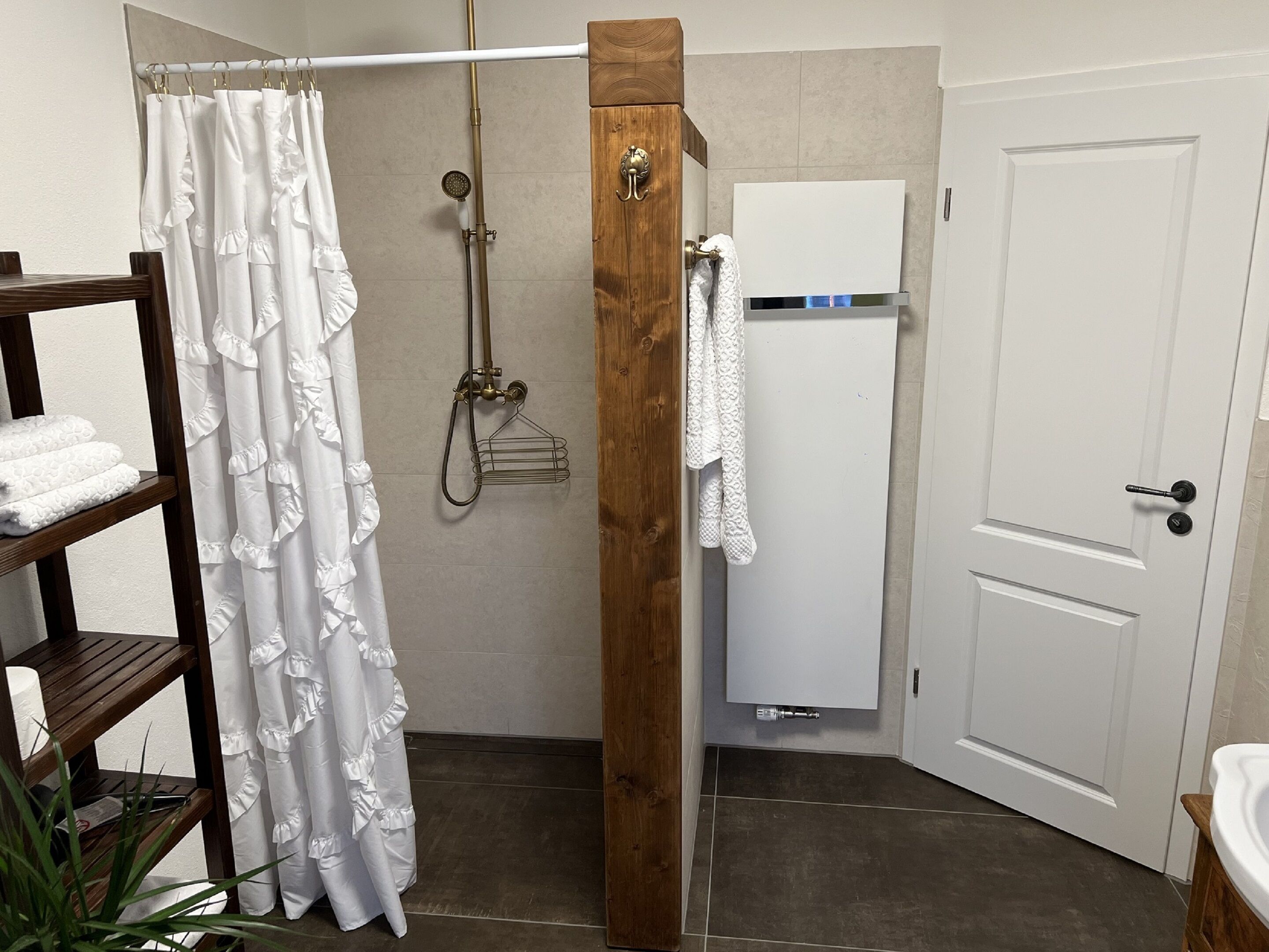 A shower with a wooden post, a white towel rack, and a white towel hanging on the wall.