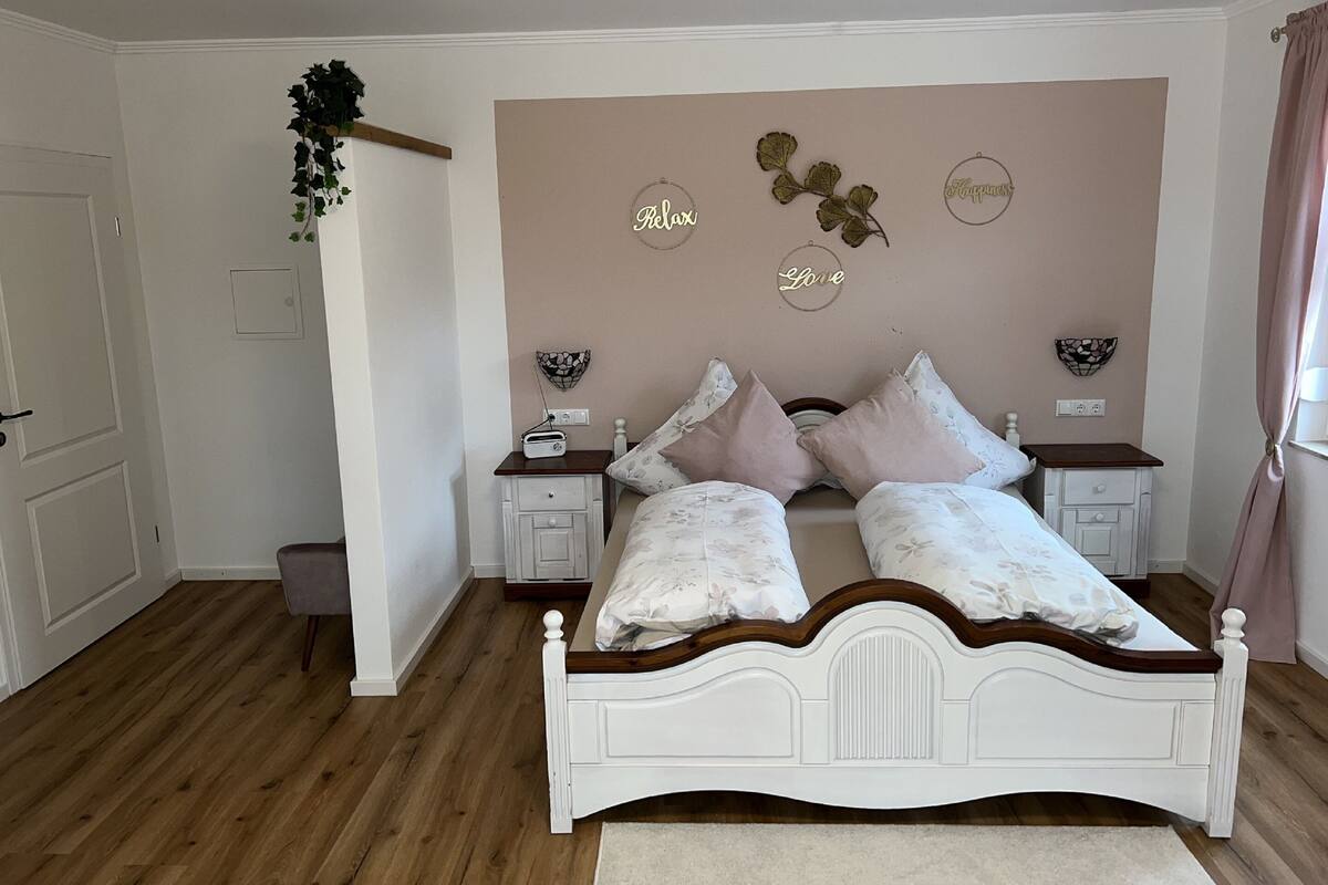 A bedroom with a double bed, two bedside tables, a nightstand, a wall-mounted radio, and decorative wall art.