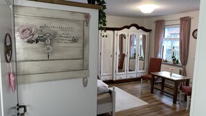 A room with a bed, a wooden floor, a white wardrobe, a chair, a table, and a window with curtains. - Der Moserhof (Oberaurach)