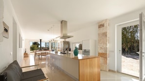 A modern kitchen with a central island, a dining area with chairs, and a large window providing a view of the outdoors.