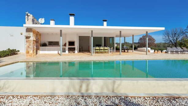 A modern house with a swimming pool, outdoor seating, and a stone facade.