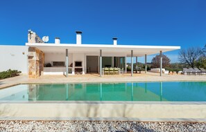 Ein modernes Haus mit Swimmingpool, Sitzgelegenheit im Freien und einer Stein-Fassade.