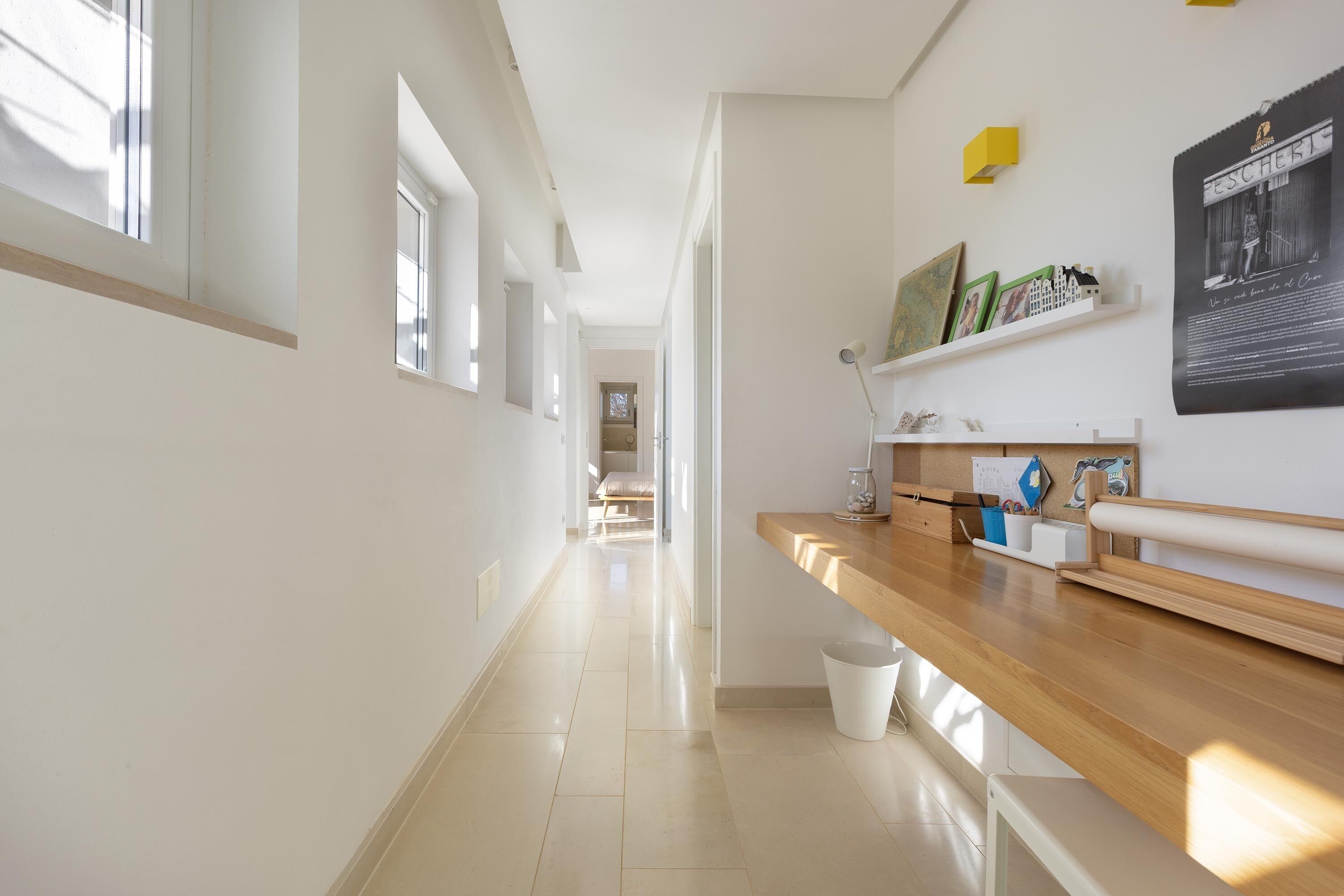 A bright hallway with a wooden counter, a white trash bin, and a framed poster on the wall.