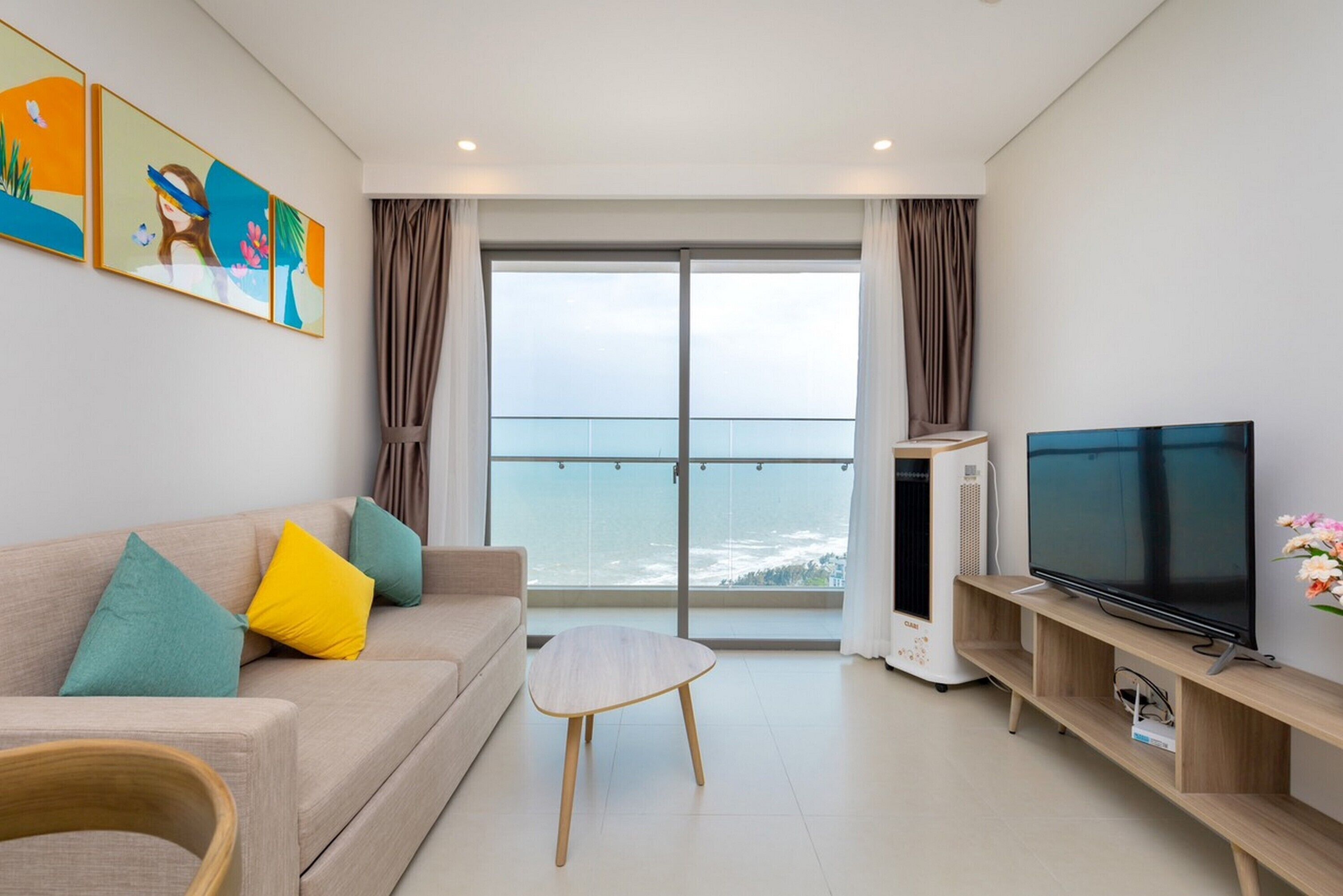 A modern living room with a sofa, a coffee table, a TV, and a balcony with a view.